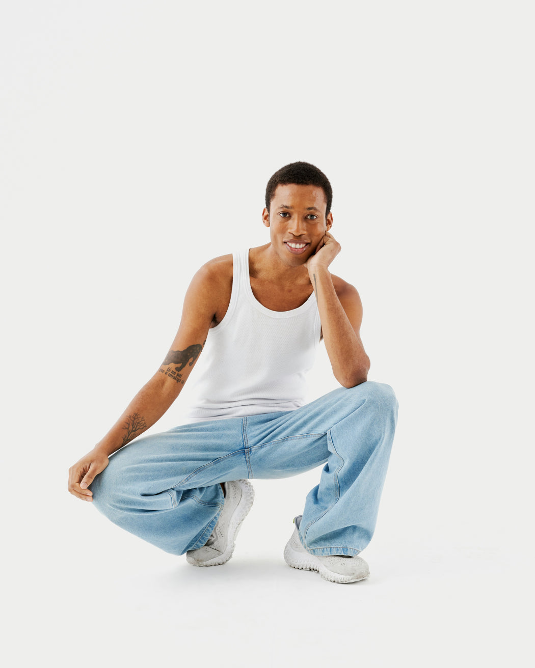 Person squatting in white tank top and light blue jeans on white background