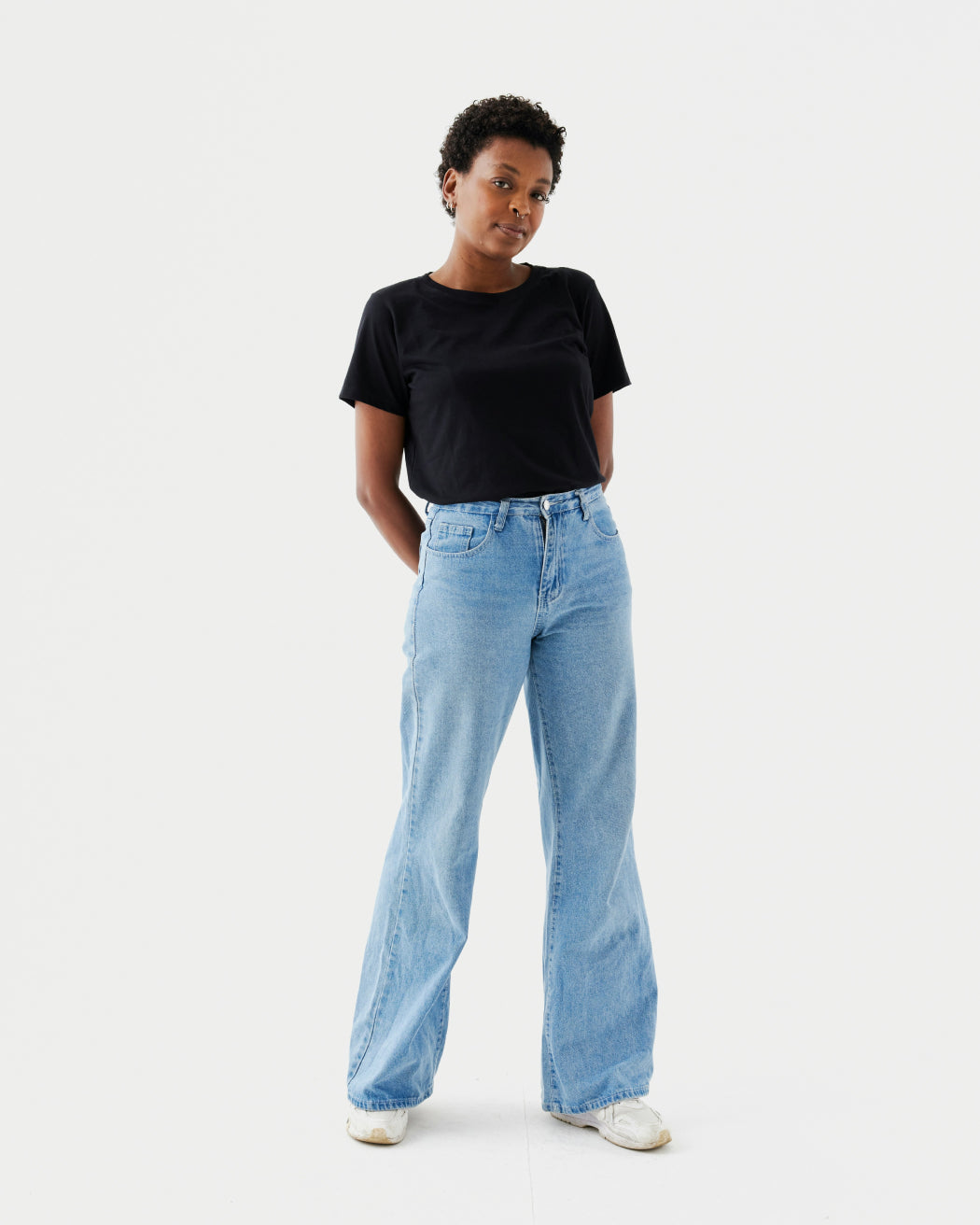Person standing in black t shirt and wide leg light blue jeans on white background