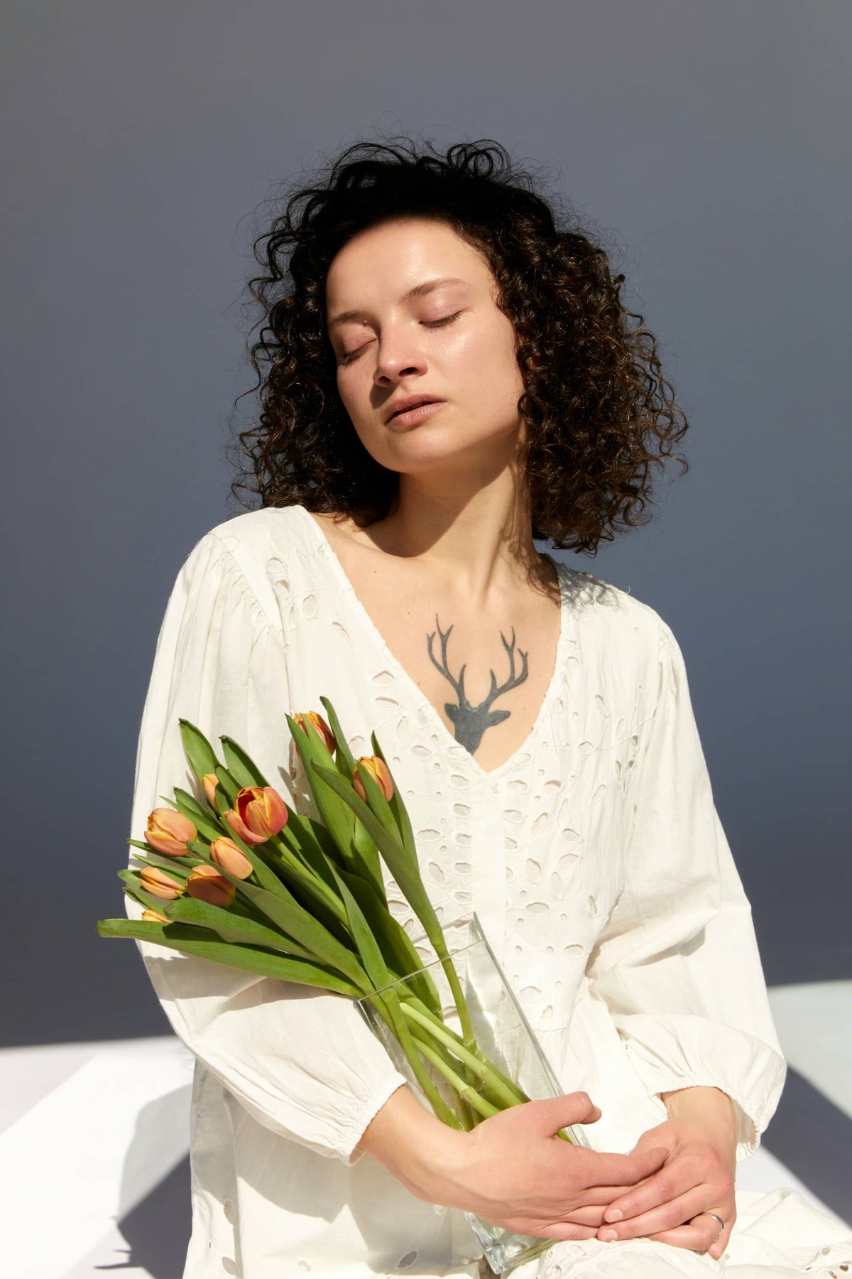 Woman in white dress holding bouquet of tulips with deer tattoo on chest