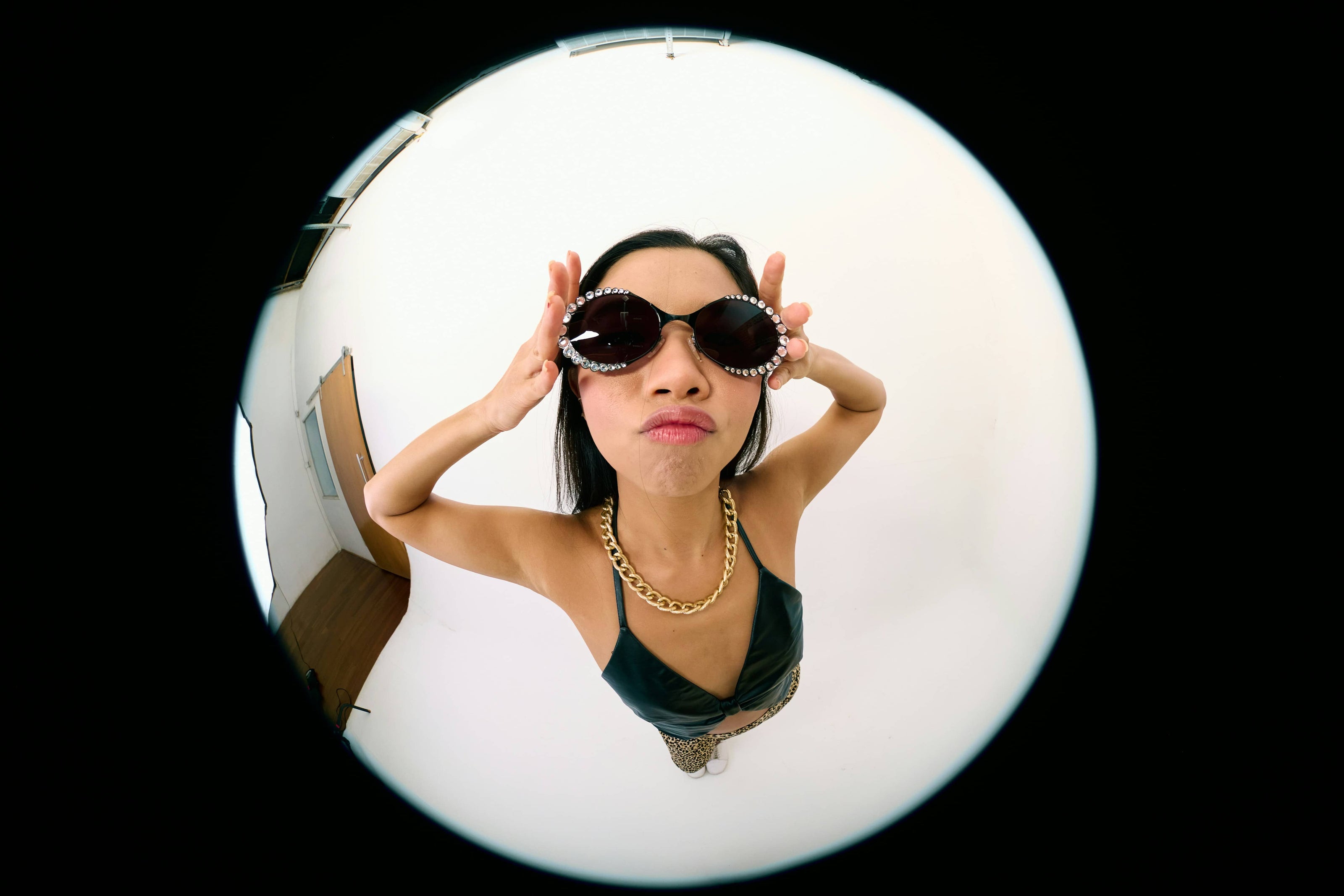 Model wearing oversized embellished sunglasses and gold chain necklace shot with fisheye lens