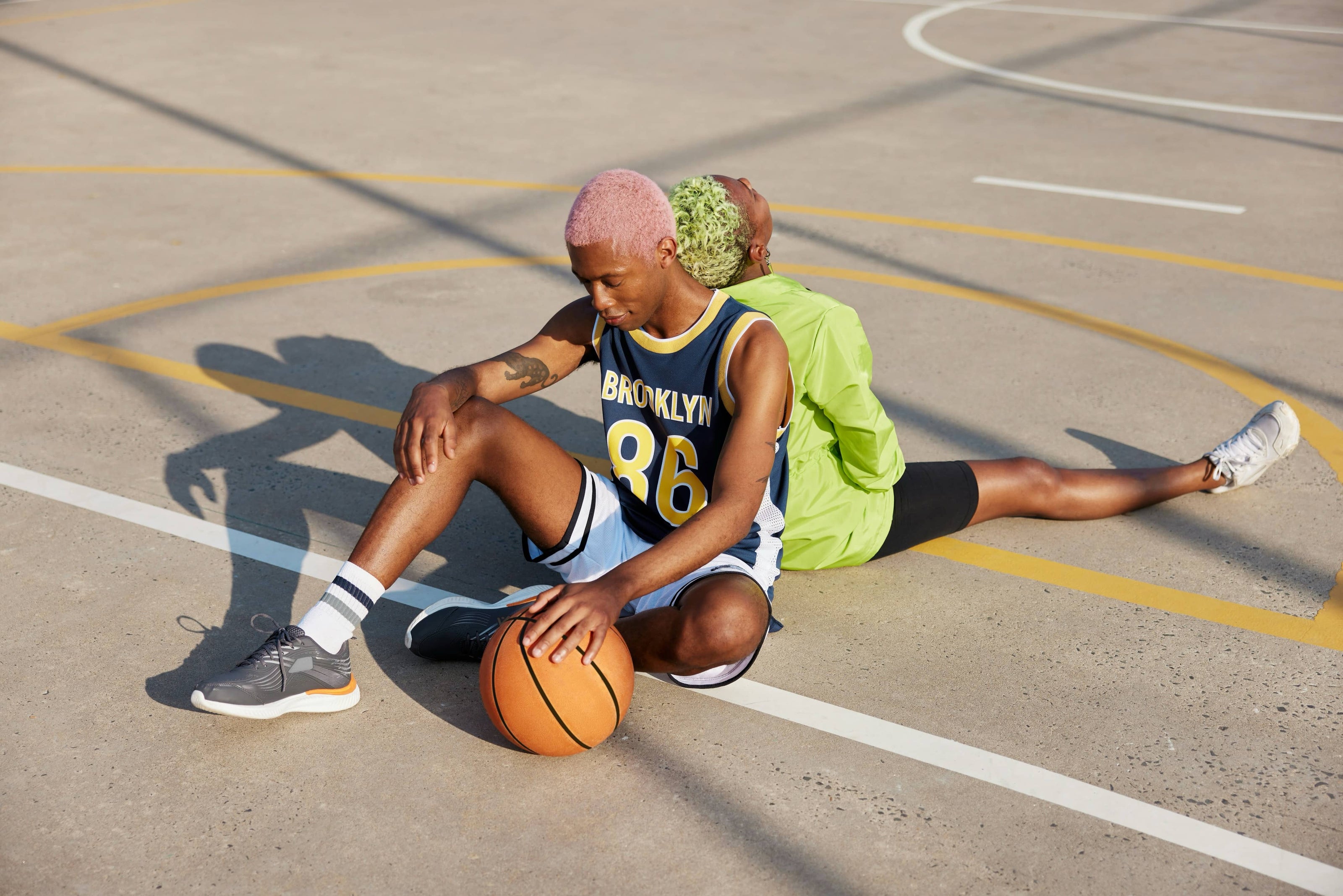 Two people sitting back to back on outdoor court with basketball