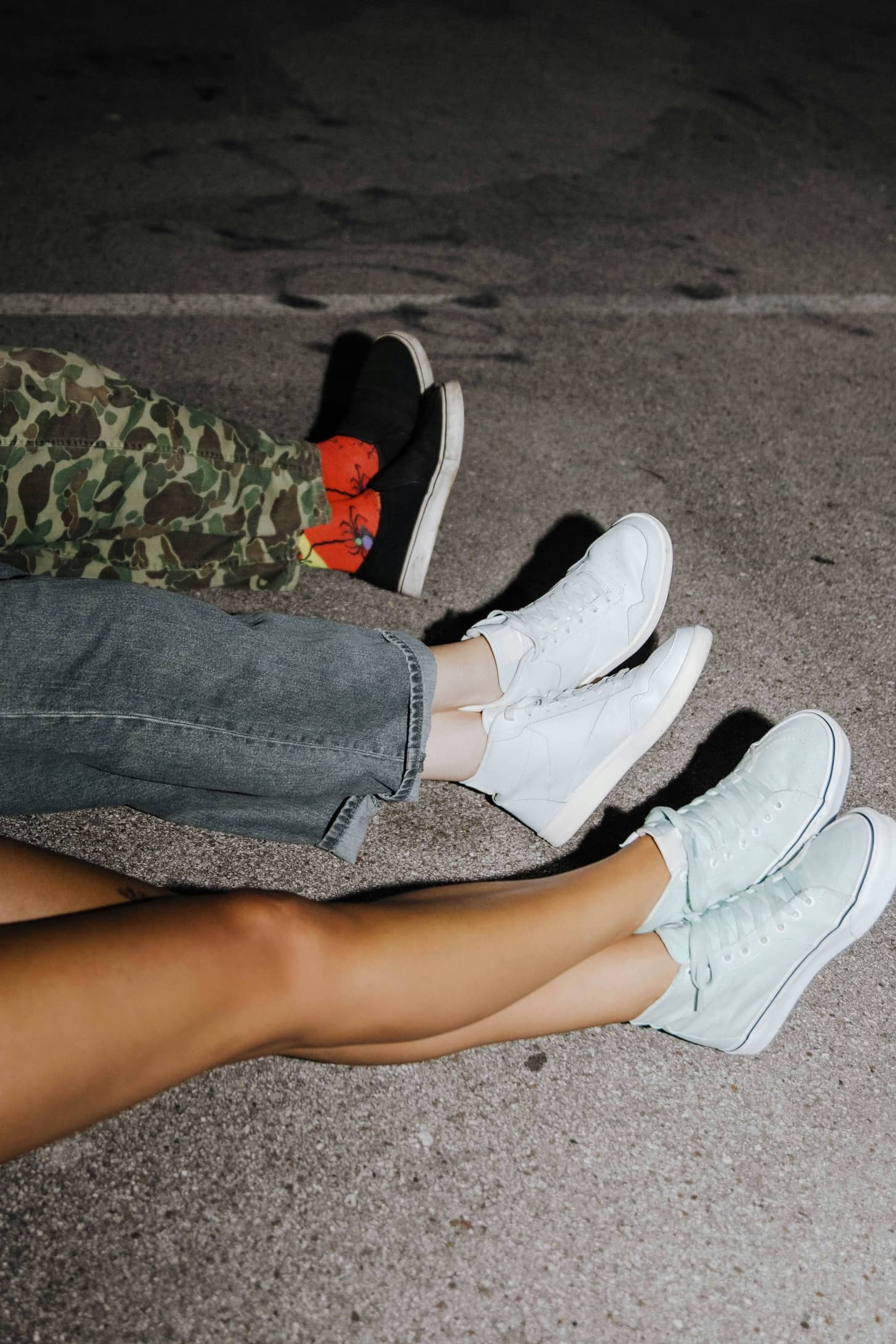 Three people sitting on pavement wearing casual sneakers